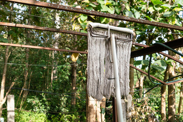 Mop hanging on a wire with forest in the background. Dirty wet mop with metal handle are drying on a wire.