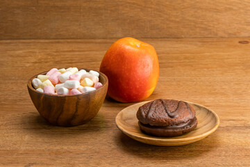 Cocoa Marshmallow Chocolate Cake in wooden plate with Marshmallow in wooden bowl and red ripe apple on wooden table.