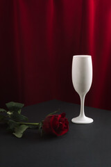 Minimal vintage style concept with white wine glass and red rose. Silk red curtain background....