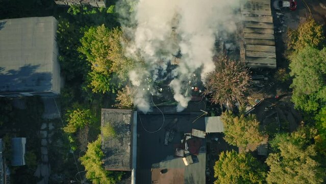Team 911 is putting out a fire in the warehouse - an airial drone shot. Smoke from the fire rises into the sky - smoke in warehouse in the city.
