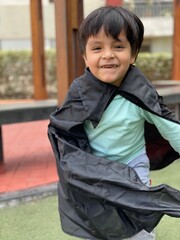 Niño Feliz con capa negra en el parque de su casa 