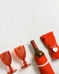 Festive table setting for Valentines Day with red glass colored wine glasses, bottle of red wine, linen napkins on table, copy space, flat lay. Concept Holiday home dinner 14 february day