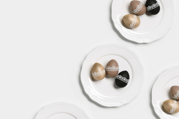 Easter eggs golden, black and beige colored in white plate, pattern on white background. Symbol Easter holiday, dyed chicken egg bright trendy colors and decorated lace tape. Top view