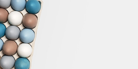 Easter eggs pastel colored in egg box on light background with copy space. Minimal Easter celebration concept, dyed chicken egg with color gradient from blue to beige coloured in carton pack