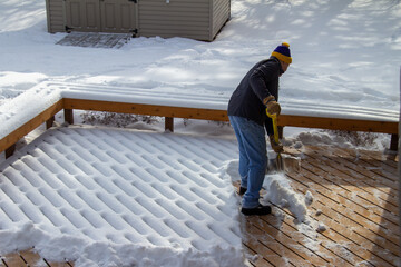 Adult male shoveling fresh new snow that has interesting geometric designs, on a wooden deck in winter