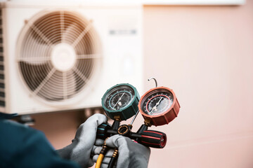 Mechanic air conditioner technician using manifold gauge checking refrigerant for filling home air...