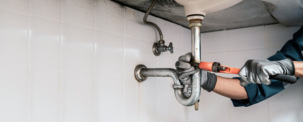 Technician plumber using a wrench to repair a water pipe under the sink. Concept of maintenance, fix water plumbing leaks, replace the kitchen sink drain, cleaning clogged pipes is dirty or rusty.