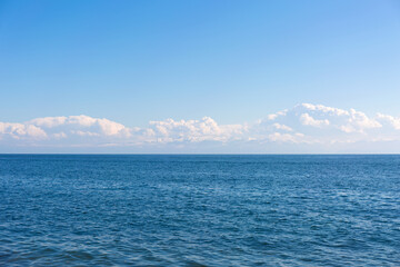 Fototapeta na wymiar Blue calm sea and white clouds. Snow capped mountains on the horizon.