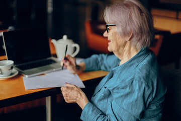 Happy senior woman sitting in a cafe with a cup of coffee and a laptop Retired woman chatting unaltered