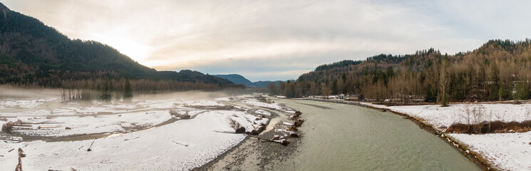 Aerial Panoramic View of Chilliwack River with snow during winter season. Cloudy Sunset Sky. Fraser Valley, British Columbia, Canada.
