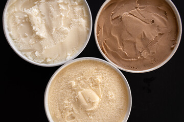 Botes de helado de varios sabores, toma picada, fondo negro. 