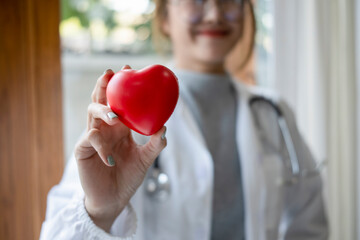 Smiling female doctor with stethoscope holding red heart shape in hand. Healthcare and medical concept.