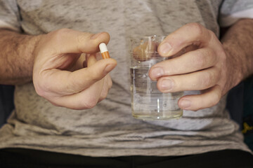 a man is holding a pill and a glass of water in his hands close-up