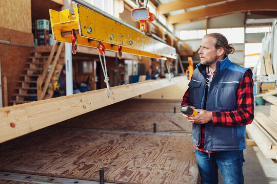 Worker in a timber factory controlling a hoist lifting a beam