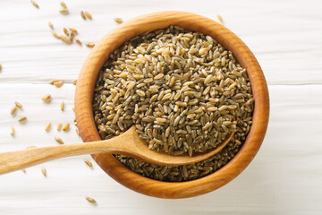 Uncooked, raw freekeh or firik, roasted wheat grain, on wooden plate with wood spoon on white rustic table. Horizontal top view from above