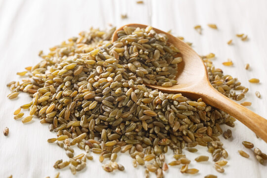 Wooden spoon with roasted Freekeh grains on white rustic table. Horizontal