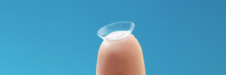 Soft contact lens on female finger on blue background
