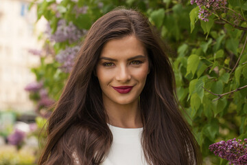 Naklejka premium Close-up portrait of beautiful young lady with long healthy brown hair smiling looking at camera in park in spring. Nature, people and happiness concept.