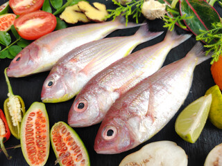 Fresh Pink Perch (thread finned Bream) Decorated with vegetables on a wooden pad,Black Background,Selective focus