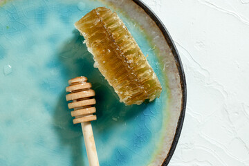 Sealed honeycomb of honey with wooden Honey Dipper for mixing and tasting natural honey on a blue porcelain plate on a white table