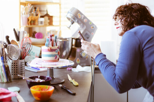 Caucasian woman at home taking a picture of a cake with her mobile phone. Selective focus.