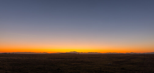 incredible sunset and blue hour over a flat landscape with mountains on the horizon panorama