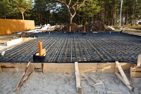 Iron fittings on a wooden formwork with laid pipes are the basis for pouring the foundation of the house with a concrete slab. Construction of cottages, design, engineering communications.