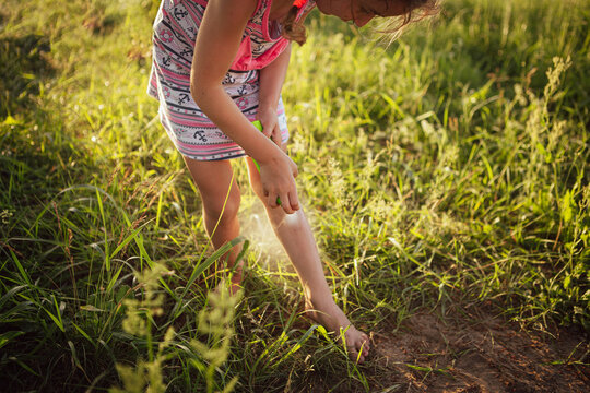 Girl sprays mosquito spray on the skin in nature that bite her hands and feet. Protection from insect bites, repellent safe for children. Outdoor recreation, against allergies. Summer time