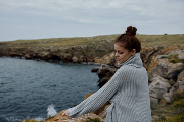 Fototapeta premium woman in a gray sweater stands on a rocky shore nature Lifestyle