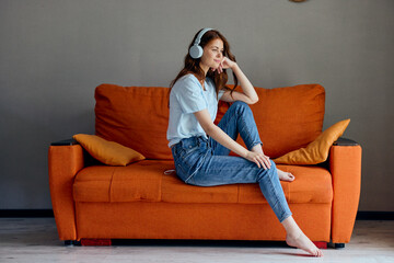 Obraz premium woman on the orange sofa listening to music with headphones technologies