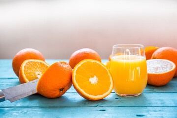 Knife splitting an orange in half, glass of natural juice of several organic oranges, some whole, some squeezed, for the diet, on a blue wooden table, Healthy Breakfast