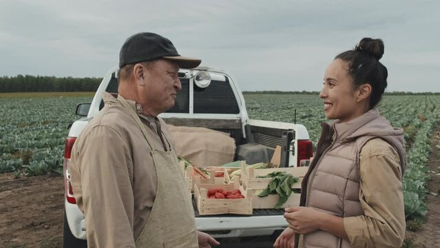Joyful young adult woman buying vegetables at farmers standing in front of farm owner talking to him and doing handshake