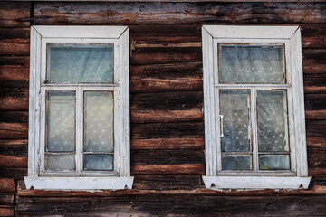 Obraz na płótnie Canvas two wooden white windows with glass in a wooden log house. Background, splash screen. Tver, Russia. 