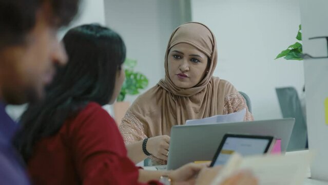 Young Indian Muslim woman and friend discussing with laptop.Asian man and woman group of young creative people in smart casual wear discussing business brainstorming meeting ideas design project.