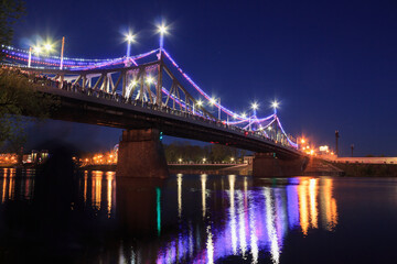 Bridge across the Volga River in Tver, evening, lights are on, many people are standing on the bridge.