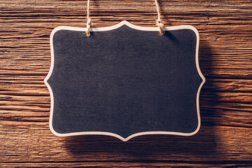 Empty black chalkboard sign hanging on rope on wood background