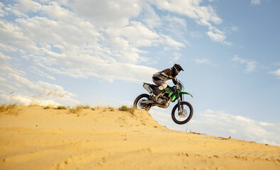 Professional motocross rider sliding down sand hill