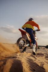 Motocross rider skidding wheel raising sand dust