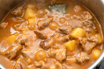 Pork meat is stewed in a saucepan with potatoes and bay leaves in gravy.