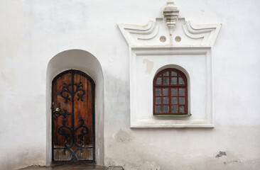 Beautiful architecture of the rear entrance into the old church, antique door and latticed window in a white church wall