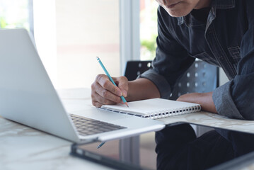 Close up of asian casual business man searching information on laptop computer and writing notes on...