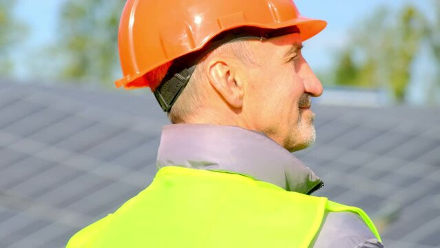 Solar station provides clean power at farm. Satisfied builder in orange hardhat examines modern installed sun panels closeup