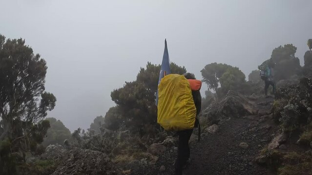 A group of black porters with backpacks and trunks on a mountain path on the way to Kilimanjaro. View from the back. Climbing Kilimanjaro, Tanzania, Africa. Raindrops on camera.
