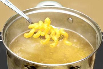 boiled hot pasta in a spoon over a pot of boiling water