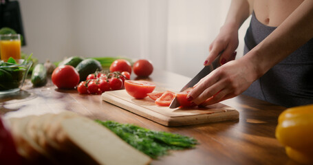 Close up of woman's hands cutting juicy fresh tomatoes on wooden chopping board. Fit lady with slim body making salad. Healthy eating concept.