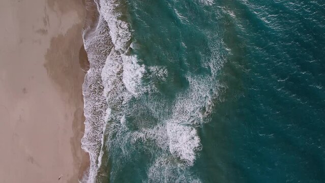 Deserted beach aerial video. Sea waves roll on the sandy shore.