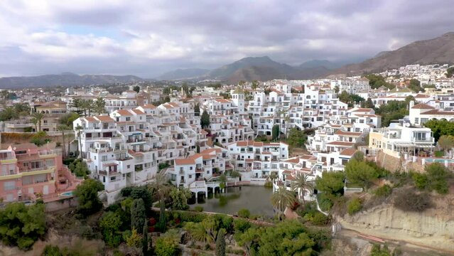 Beautiful and idyllic city of Nerja situated on Costa del Sol, Malaga, Spain. One of the most popular touristic attraction on Costa del Sol. Perspective from above. Drone  forward. Cloudy sky