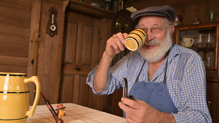 Alter Mann Weinbauer trinkt Wein oder Most aus einem Krug und raucht Pfeife und lächelt.