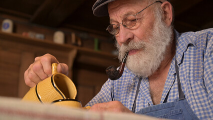 Old man winegrower drinks wine or cider from a jug and smokes pipe and smiles. A retired pensioner...