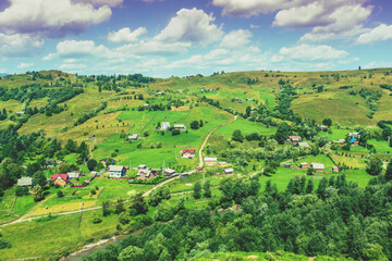 Fototapeta na wymiar View of countryside in summer. Village on the hills with beautiful cloudy sky